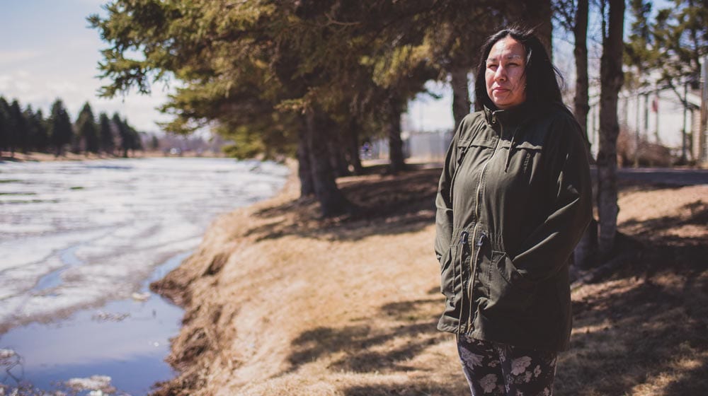 Cheryl Suggashie stands at the McIntyre River where her brother Clayton Mawakeesic was found dead in 2015.